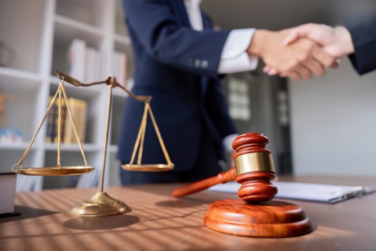 Judge gavel and scales of justice on a desk while two people shake hands