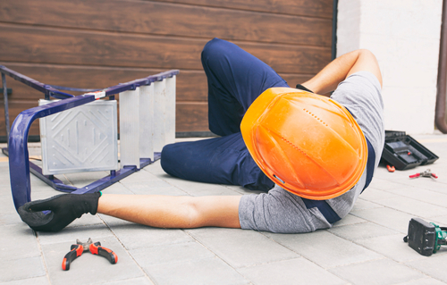 Construction worker wearing a hard hat lying on the ground after a ladder fall.