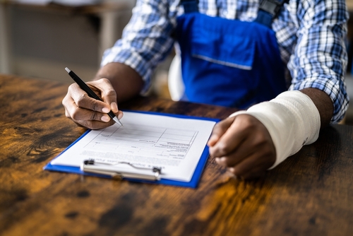 Injured worker with a bandaged arm filling out paperwork at a desk.