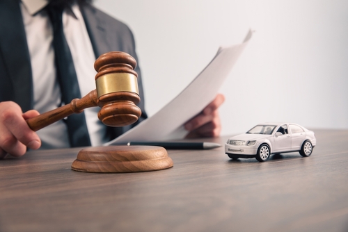 Close-up of a lawyer in a suit reviewing legal documents at a desk with a gavel and a small toy car, symbolizing car accident law and personal injury cases.