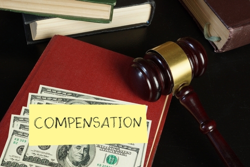 Gavel and cash placed on a red law book labeled “compensation,” representing financial recovery in a workplace injury or legal claim.