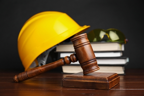 A yellow construction hard hat sits beside a judge&rsquo;s gavel and stacked law books, symbolizing workplace injury law and workers&rsquo; rights.