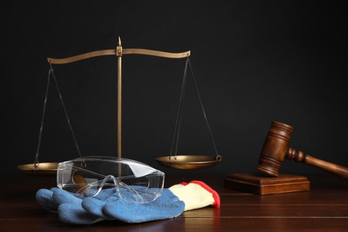 Safety gloves and goggles resting on a judge’s gavel and scales of justice, symbolizing workplace safety and legal protection.