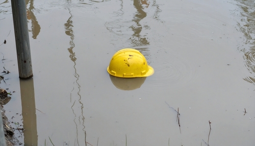 Yellow construction hard hat floating in muddy water at a worksite.
