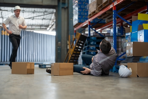 Warehouse worker sitting on the floor after slipping and falling, with boxes scattered around.
