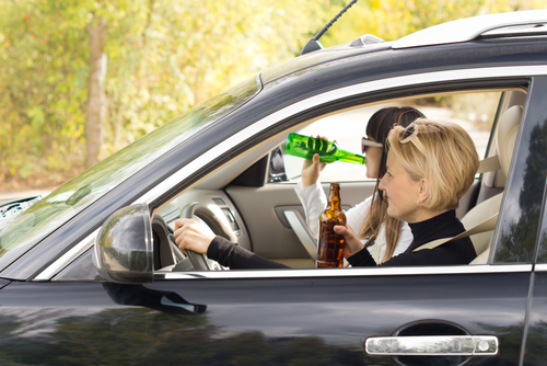 Houston drunk driving accident lawyer representing injuries caused by intoxicated drivers shown holding alcohol while driving a car.