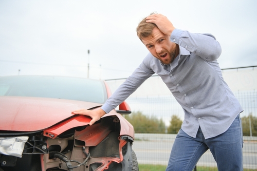 A man holding his head beside a damaged car after a crash, illustrating an accident scenario where brain injury causation may be evaluated.