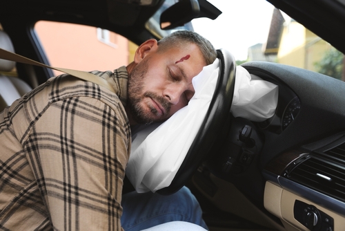 An injured driver slumped over a deployed airbag with a head wound, illustrating an accident that may lead to delayed brain injury symptoms.