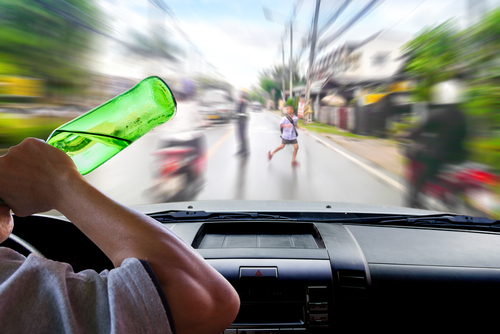 View from inside a car showing a driver holding a bottle while a child runs across the street, illustrating a case a Houston drunk driving accident lawyer may handle involving minors.