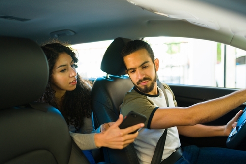A man and woman in a car, focused on their cell phones, highlighting the need for a Houston Rideshare Accident Lawyer.