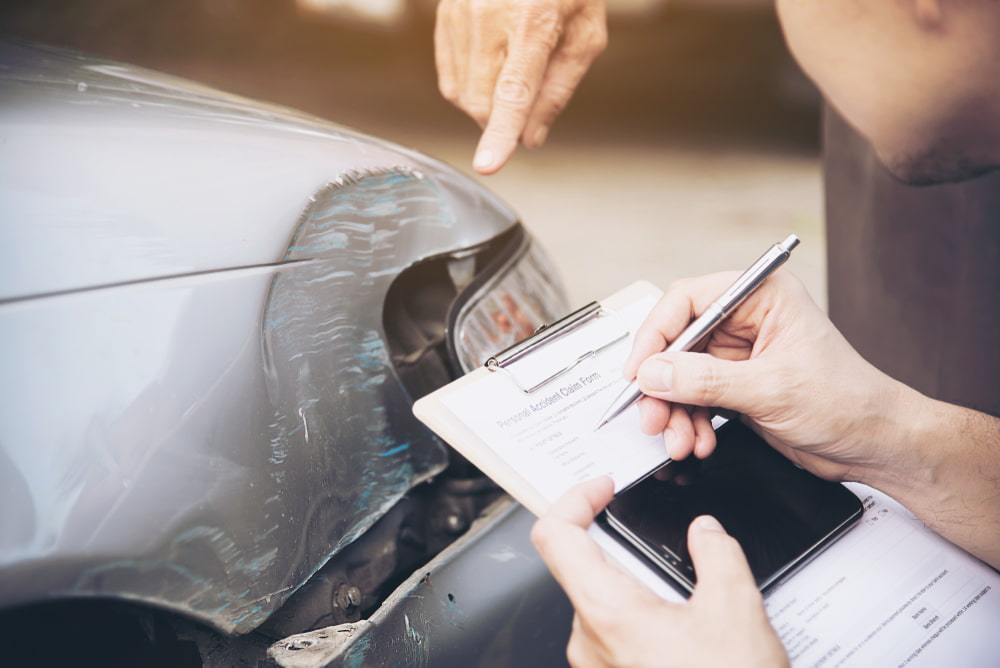 Person writing notes on a clipboard while inspecting damage on a car