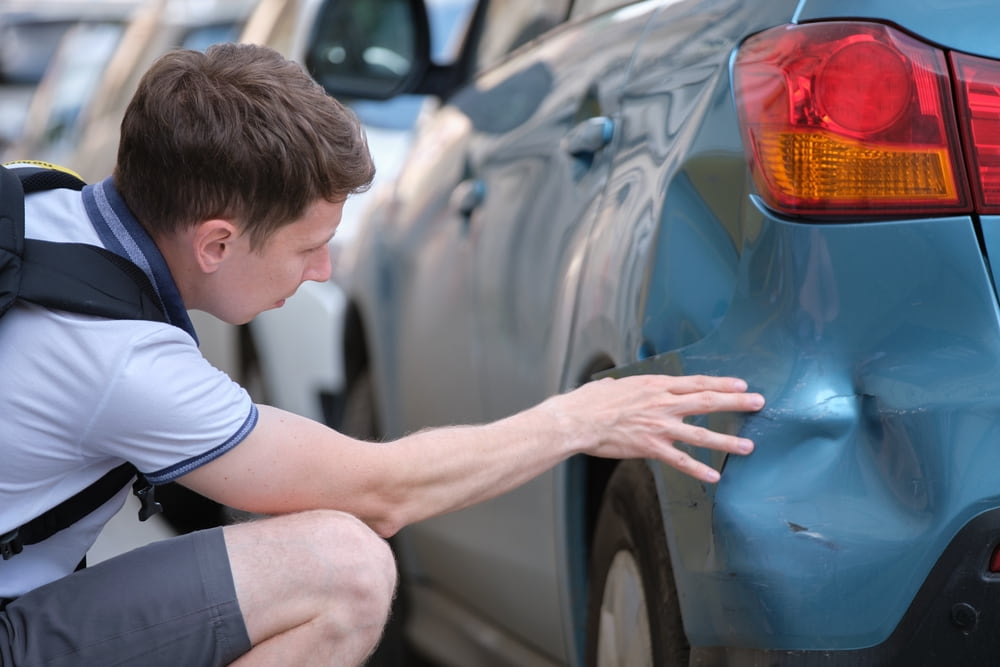 Driver examining a dented rear bumper after a car accident