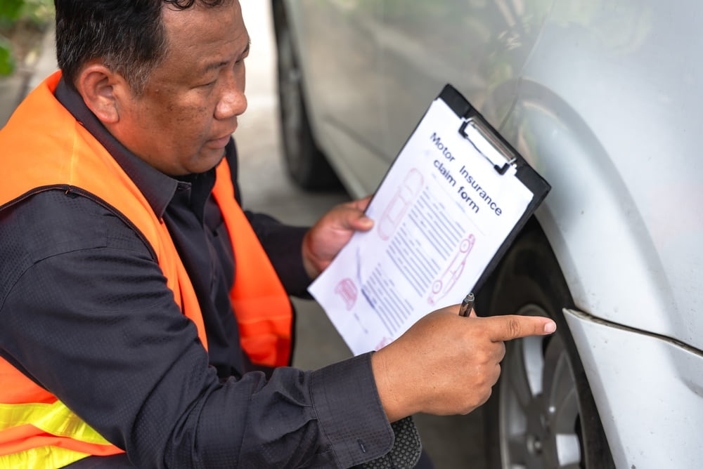 Insurance adjuster in a safety vest reviewing a damage report next to a vehicle